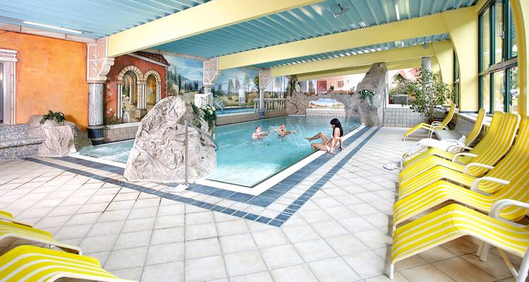 Zone de piscine intérieure de l'hôtel avec des éléments rocheux et des fresques peintes où les clients apprécient la baignade et la détente.