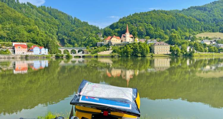 Sacoche de vélo avec carte surplombant un méandre réfléchissant du Danube et un charmant village sur la rive opposée.