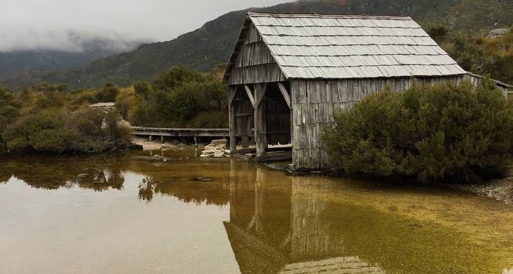Altes hölzernes Bootshaus an einem See mit Spiegelungen im Wasser.