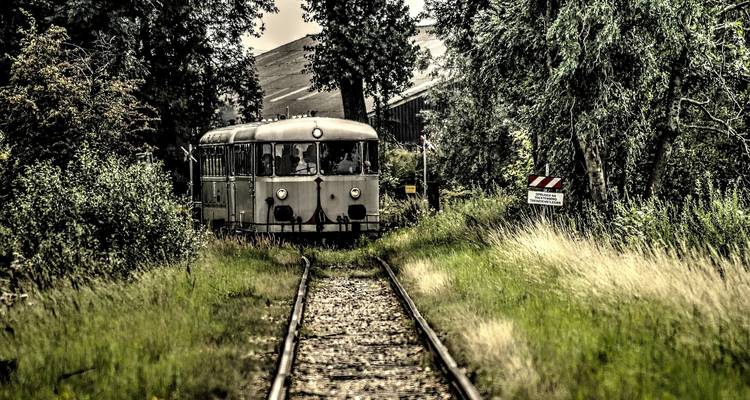 Alter Zug, der auf Eisenbahnschienen fährt, umgeben von Bäumen und Gras.