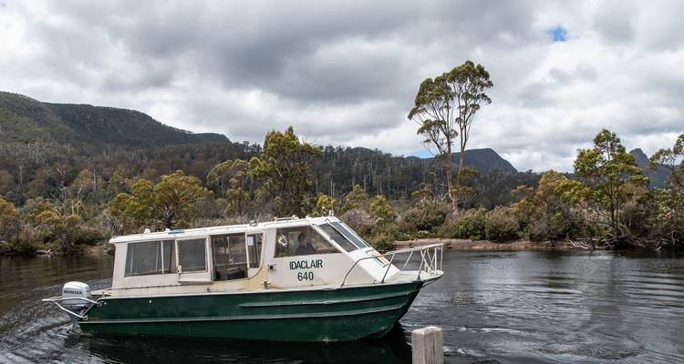 Ausflugsboot auf einem See mit bewölktem Himmel und bewaldeten Hügeln.