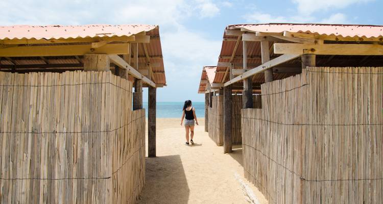 Persona caminando entre cabañas de bambú hacia la playa.