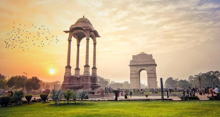 India Gate mit umliegendem Garten und Menschen bei Sonnenuntergang.