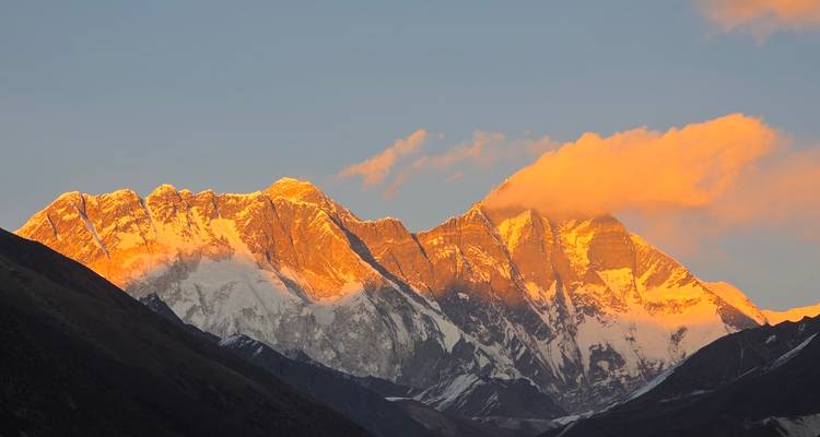 Everest massif glows with orange alpenglow as dawn light strikes the snowy summits above the valley.