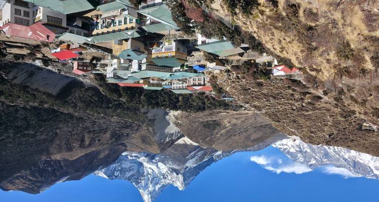 Colorful alpine village nestled beneath soaring snowy Himalayan peaks under crisp blue skies.