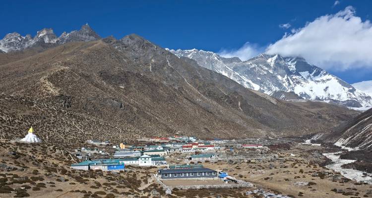 High-altitude settlement stretches along a barren valley floor below grey jagged Himalayan ridges.