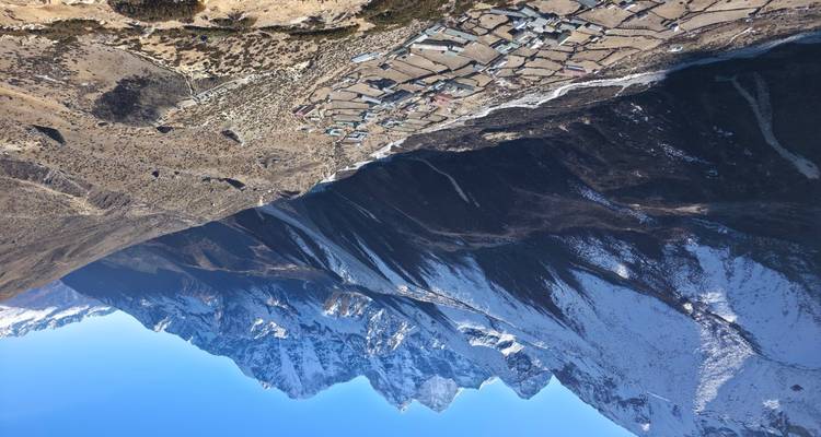 Sweeping aerial view of a long Himalayan valley village framed by dramatic snowy peaks.