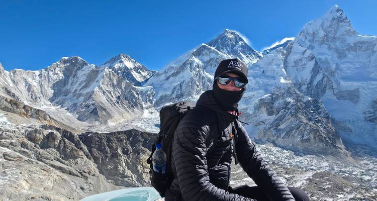 Masked climber rests on a glacier ridge with Everest skyline gleaming in his sunglasses.