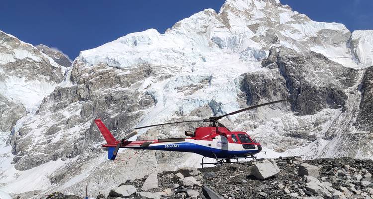 Duplicate view of red-blue helicopter on rocky ground beneath massive glacier wall.