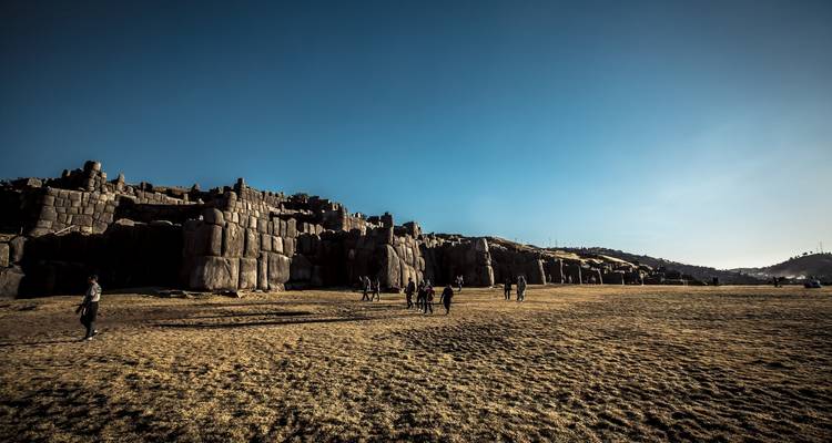 People walking in a field with ancient ruins and a landscape view.