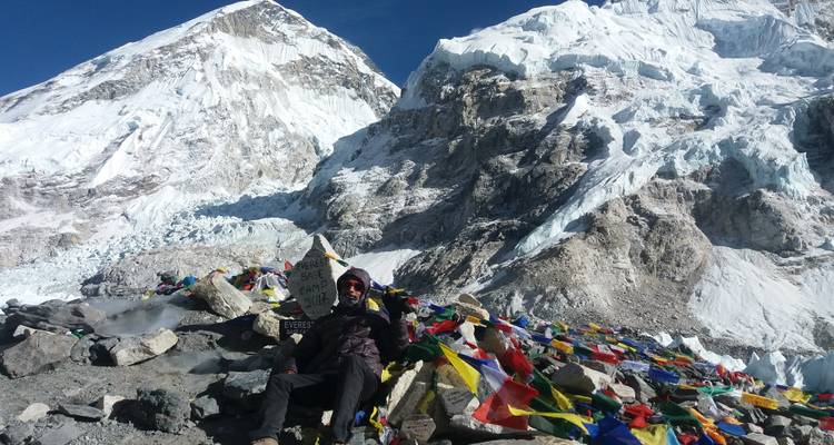Person, die mit bunten Gebetsfahnen vor einer schneebedeckten Bergkulisse sitzt.