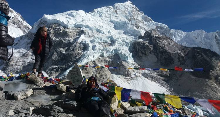 Wanderer sitzen im Everest-Basislager mit Gebetsfahnen und schneebedeckten Bergen.