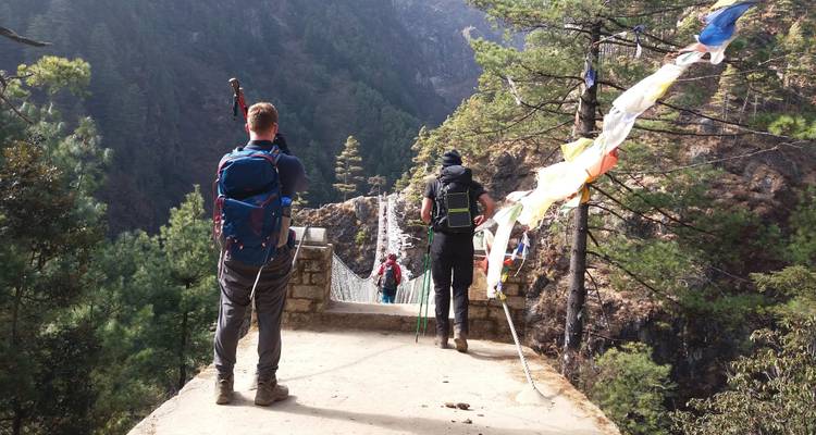 Wanderer, die eine Hängebrücke in einem bewaldeten Berggebiet überqueren.