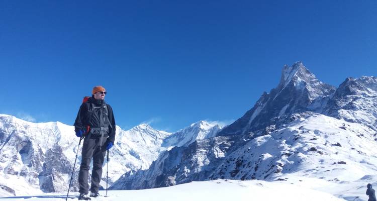 Eine Person mit Trekkingausrüstung, die in einer verschneiten Berglandschaft posiert.