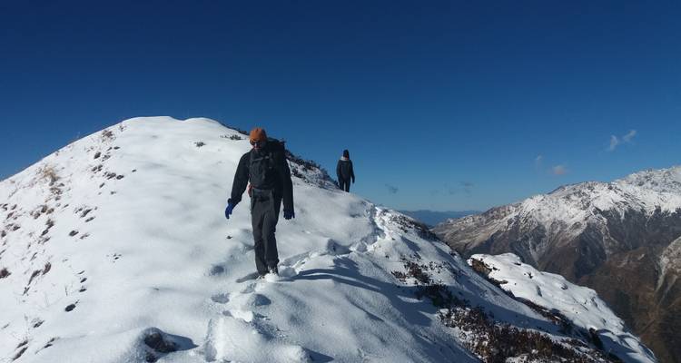 Two hikers walking along a snowy ridge with mountain views.