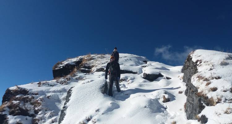 People trekking on snowy mountain terrain under clear blue skies.