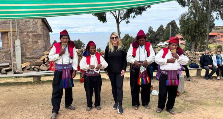 Une voyageuse pose avec des hommes vêtus de façon traditionnelle sous un auvent rayé sur le lac Titicaca.