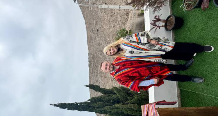 Un homme et une femme vêtus de ponchos péruviens colorés posent dans un jardin sur le toit avec des collines arides et un ciel nuageux en arrière-plan.