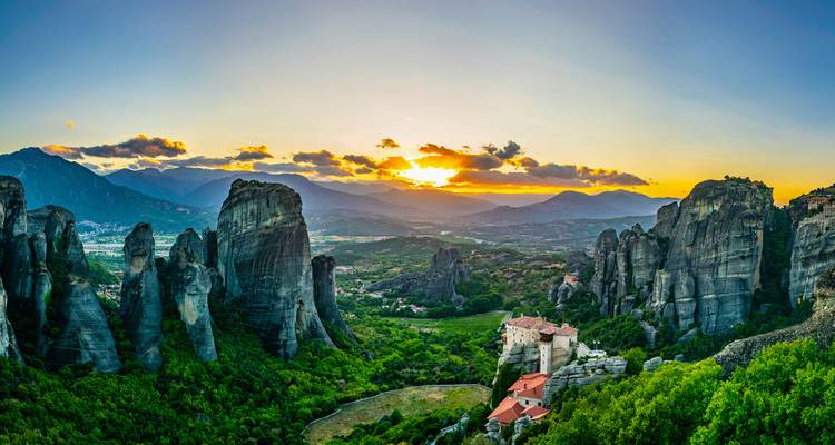 Panoramic sunset view of Meteora rock formations and monasteries.