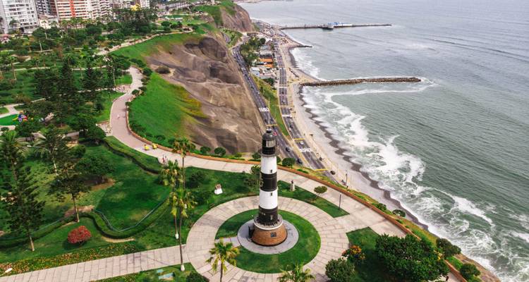 Faro situado cerca de un acantilado costero con un paseo marítimo.