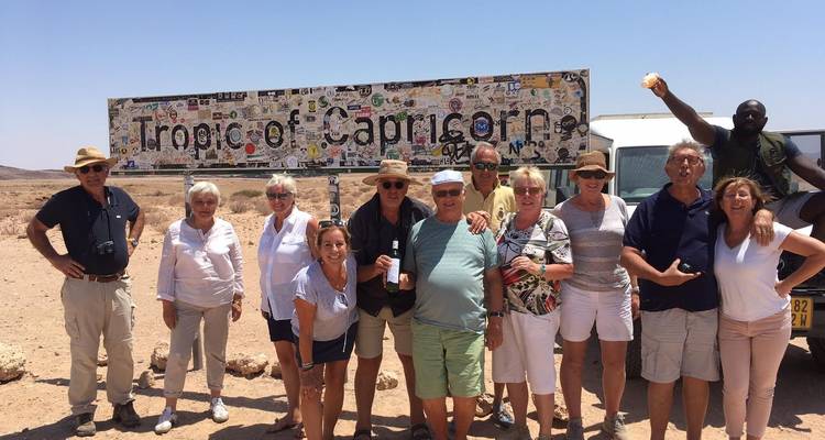 Group of tourists posing with a 'Tropic of Capricorn' sign.