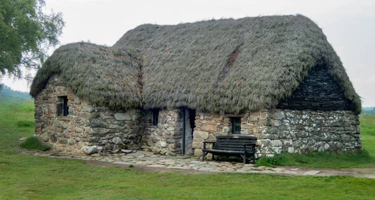 Chaumière en pierre à toit de chaume sur le champ de bataille de Culloden, entourée de pelouse verte et de ciel gris.