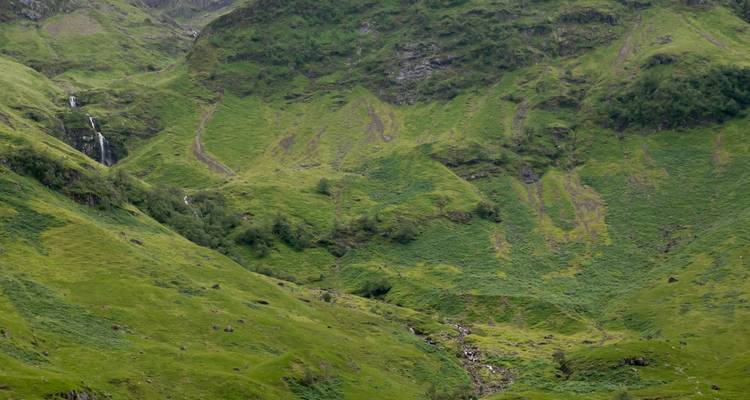 Des versants verdoyants et luxuriants ainsi qu'une cascade étroite dans la vallée des Highlands à Glencoe.