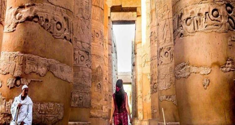 Person, die zwischen großen antiken Säulen mit Hieroglyphen steht.