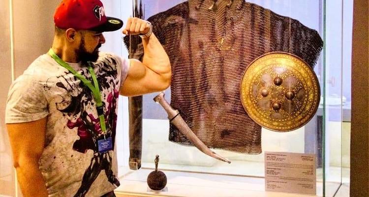 Person, die neben einer Ausstellung antiker Waffen posiert.