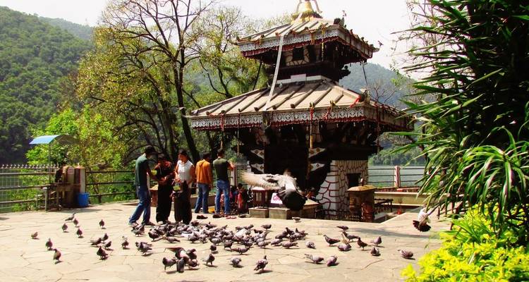 Menschen und Tauben um einen kleinen Tempel am See.