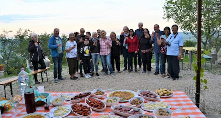 Een groep mensen poseert achter een uitgebreide maaltijd buiten.
