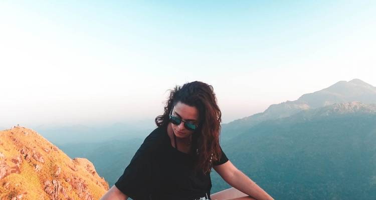 Een vrouw die op een heuveltop zit met schilderachtige bergen op de achtergrond.