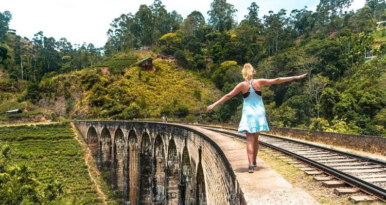 Vrouw balanserend op een spoorbrug in een schilderachtig landschap.