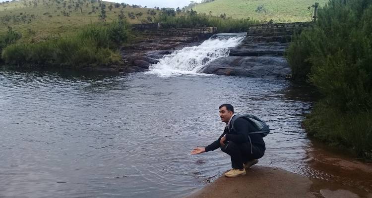 Persoon gehurkt bij een waterval in een natuurlijke omgeving.