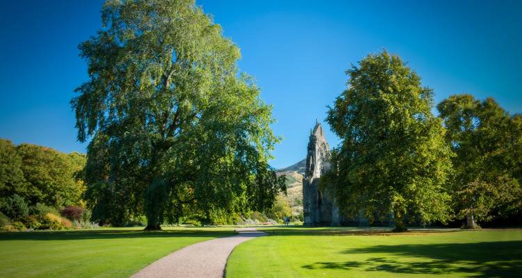 Park mit üppigem Grün und Ruinen eines historischen Gebäudes.