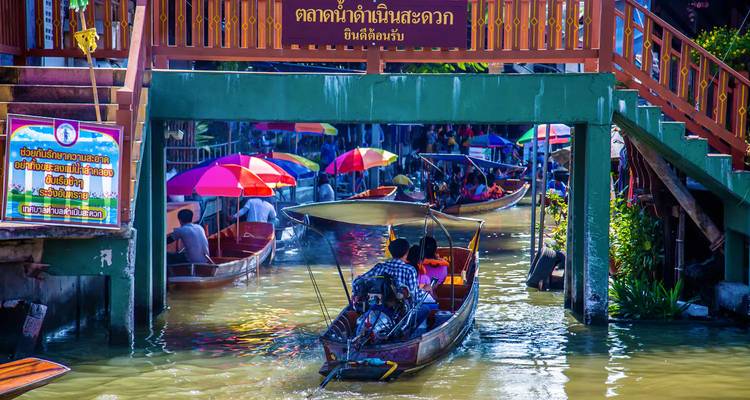 Colorful and crowded floating market with people in longtail boats beneath a bridge.