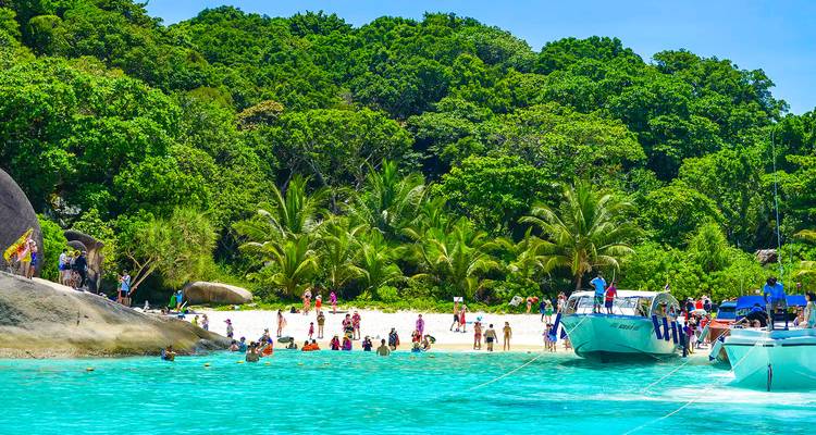 Tropical beach scene with clear waters and boats, people enjoying the beach.