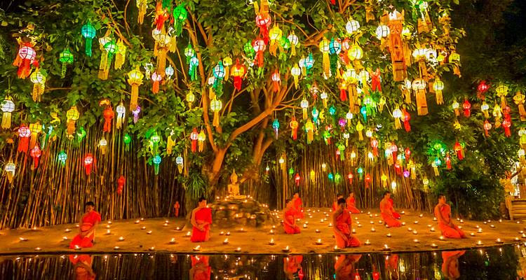Monks meditating under a tree adorned with colorful lanterns.