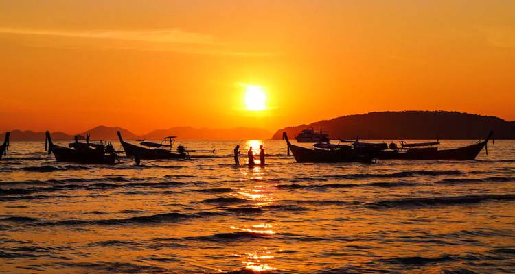 Silhouetted boats and people at sunset over the ocean.