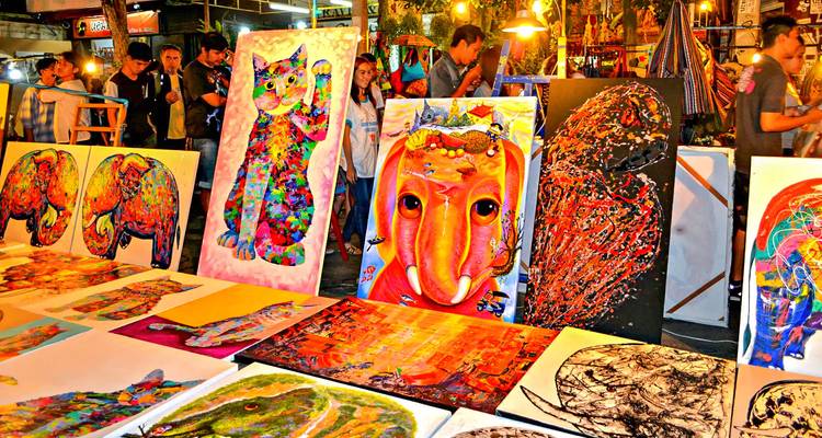 Colorful paintings and art displayed at an outdoor market.