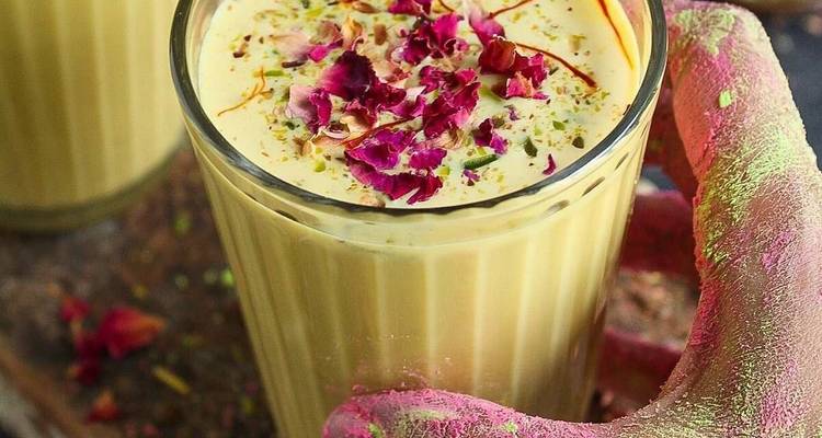 Glass of drink with rose petals held by a colorful hand.