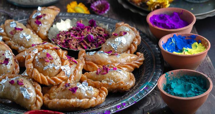 Une assiette de douceurs indiennes traditionnelles décorées de feuille d'argent et entourée de bols de poudres colorées.