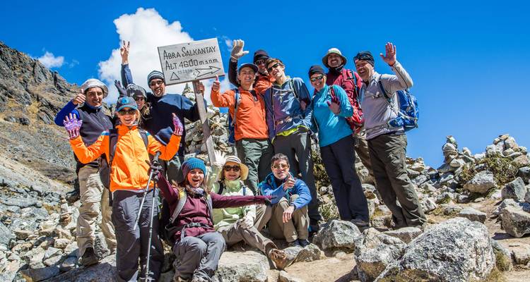 Große Trekkinggruppe, die am Schild des Abra Salkantay-Passes auf 4.600 Metern unter klarem blauen Himmel feiert.