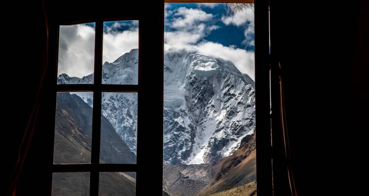 Schneebedeckter Salkantay-Gipfel, gerahmt durch ein Fenster der Lodge unter strahlenden Wolken.