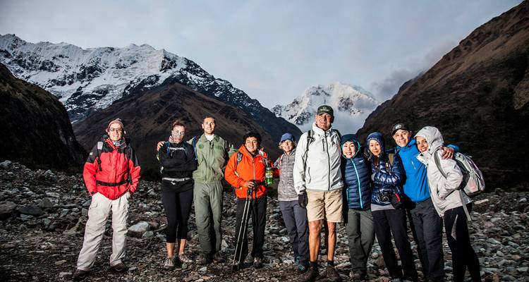 Trekkinggruppe, die sich bei Einbruch der Dämmerung auf dem felsigen Talboden mit schneebedeckten Andengipfeln im Hintergrund fotografieren lässt.