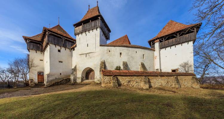 The fortified white church of Viscri with wooden defensive towers under clear blue sky.