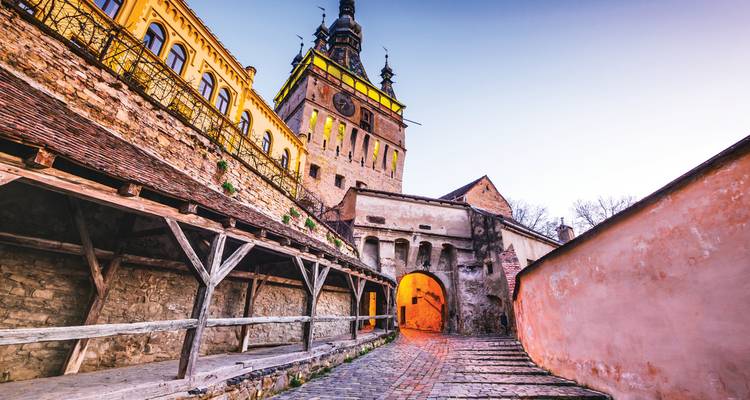 Twilight view up a covered wooden stairway to Sighisoara’s illuminated Clock Tower.