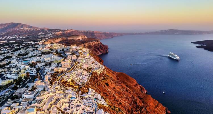Ville perchée sur une falaise avec vue sur mer au coucher de soleil à Santorin.