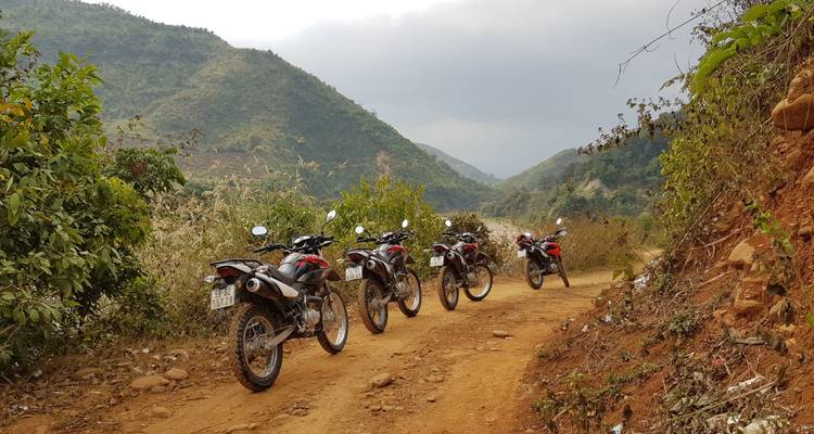 Vier motorfietsen opgesteld op een onverharde weg met bergen eromheen.