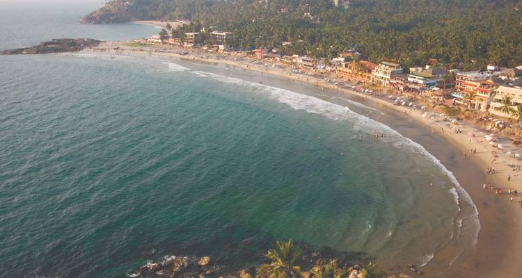 Luchtfoto van een halvemaanvormig strand met omliggende groen.